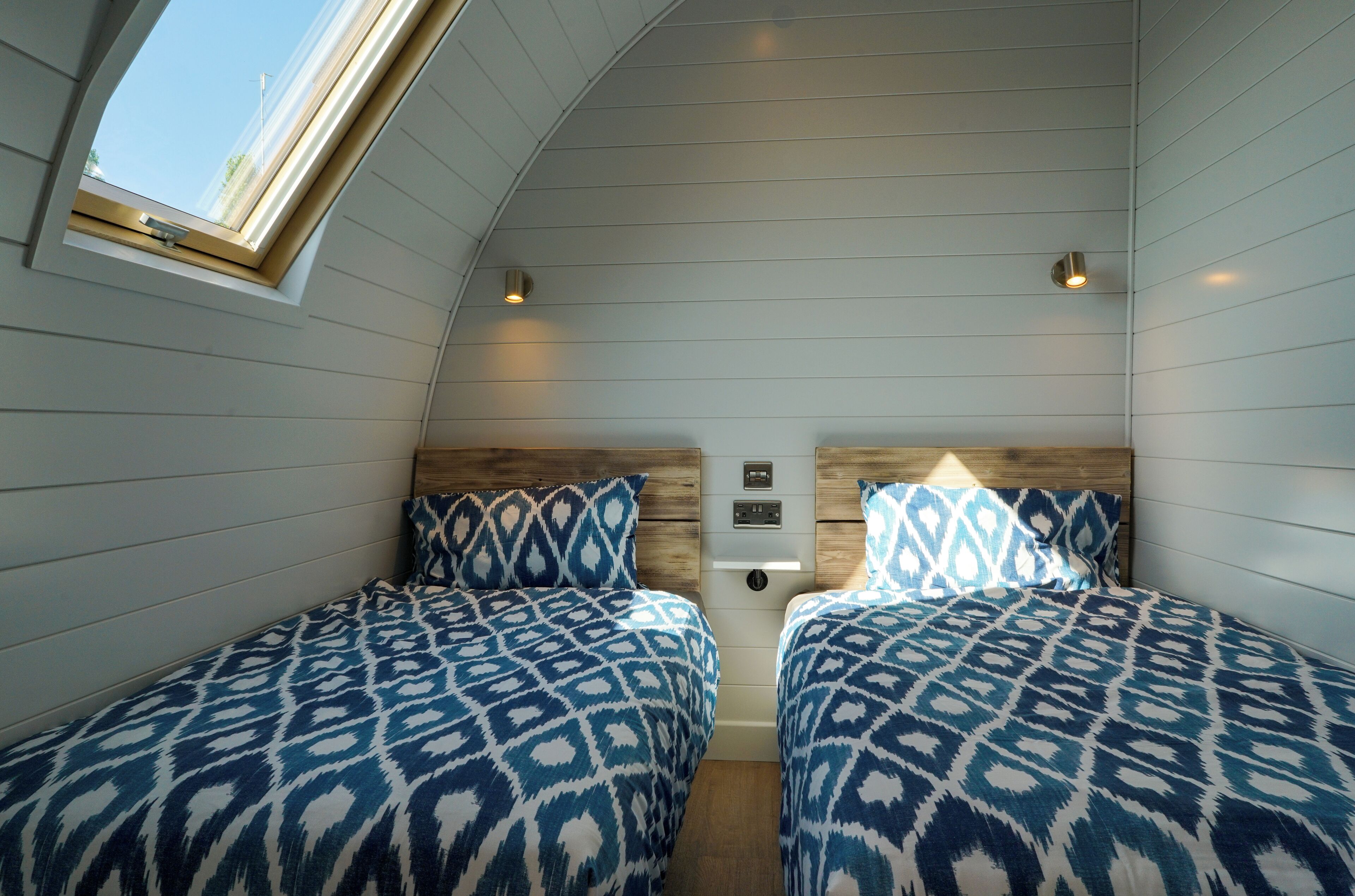 A cozy room with two beds, a skylight, and a wooden headboard.