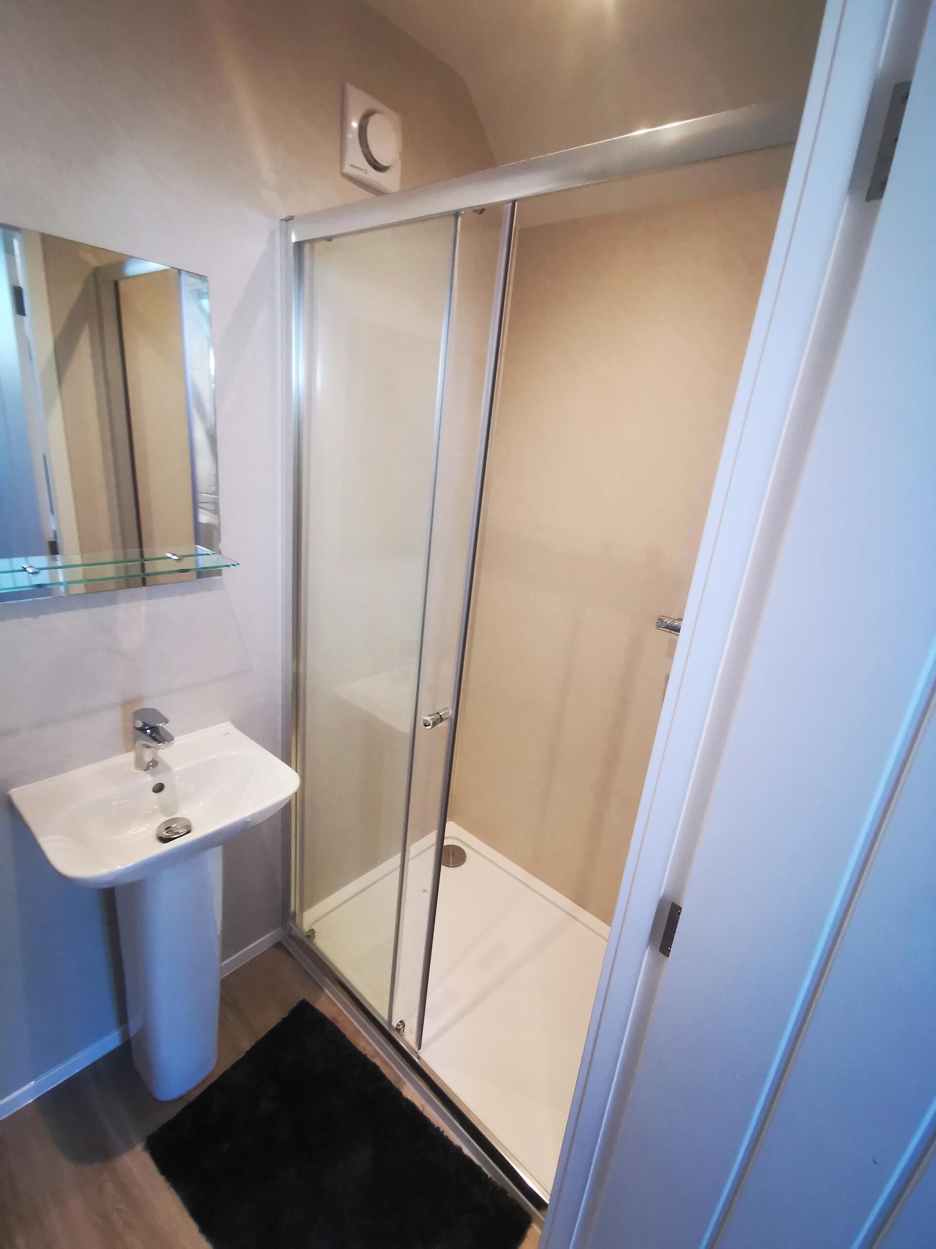 A bathroom with a glass-enclosed shower, a white sink, and a mirror above the sink.