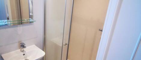 Un baño con ducha de vidrio, un lavamanos blanco y un espejo sobre el lavamanos.