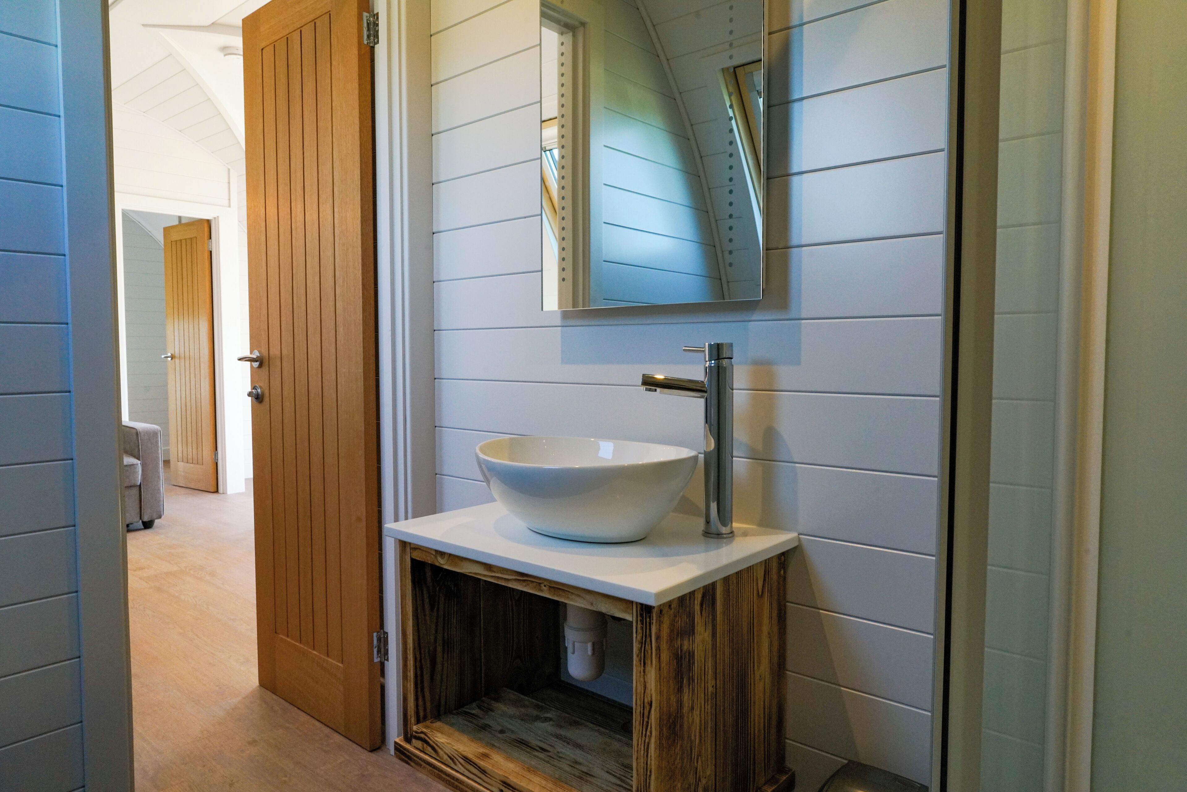 Un baño con tocador de madera, un lavamanos blanco y un espejo.