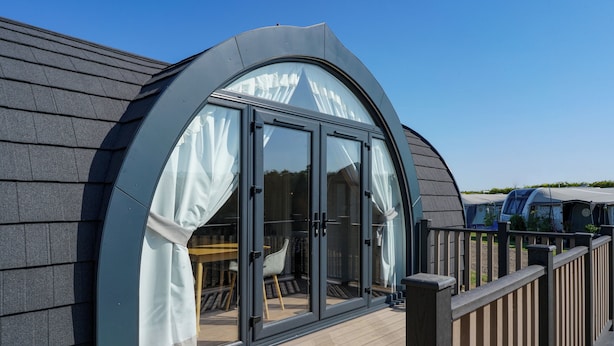 Un bâtiment moderne doté d’une grande baie vitrée incurvée et d’une terrasse en bois.