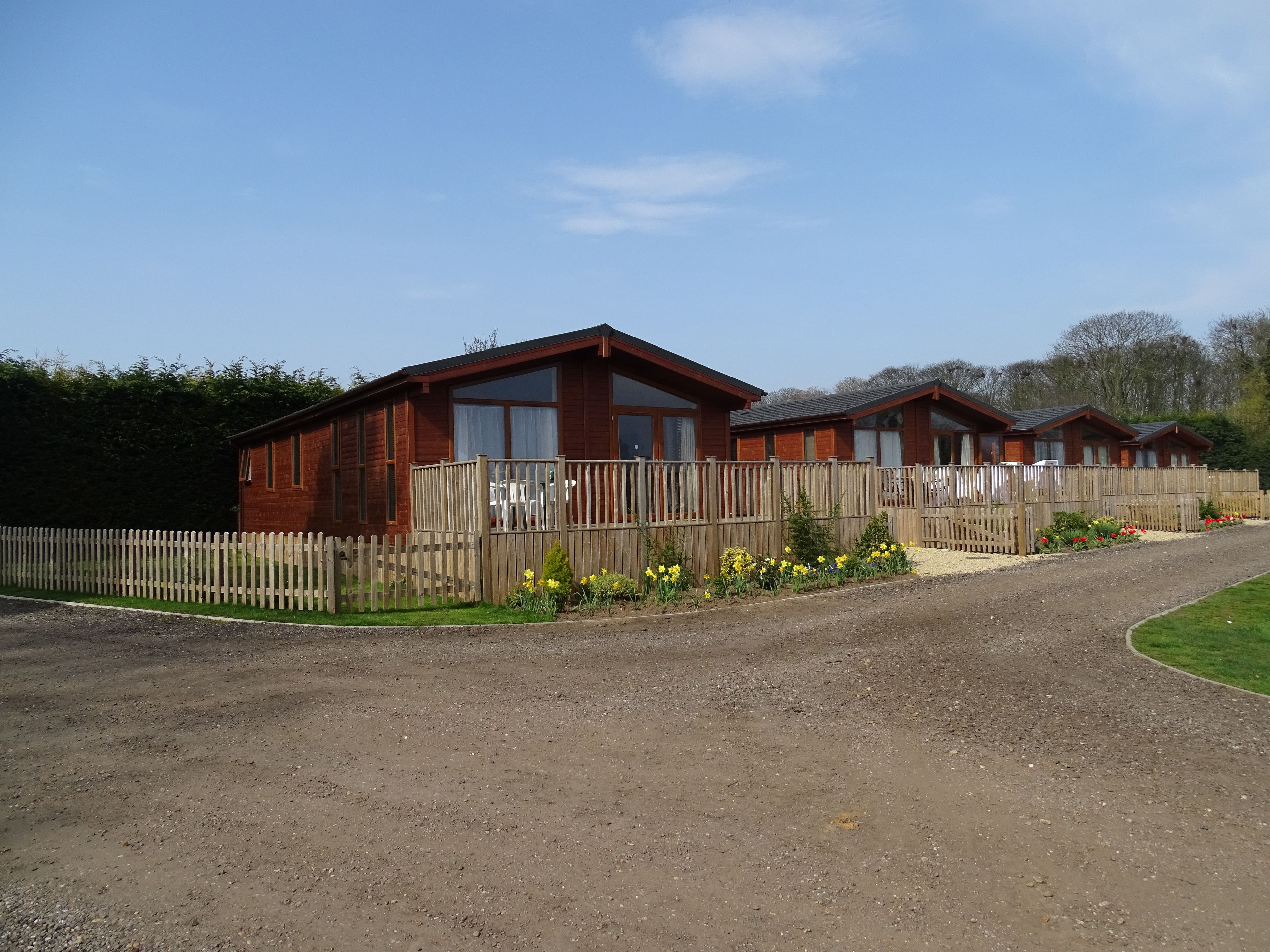 A row of wooden cabins with a gravel driveway and a wooden fence.