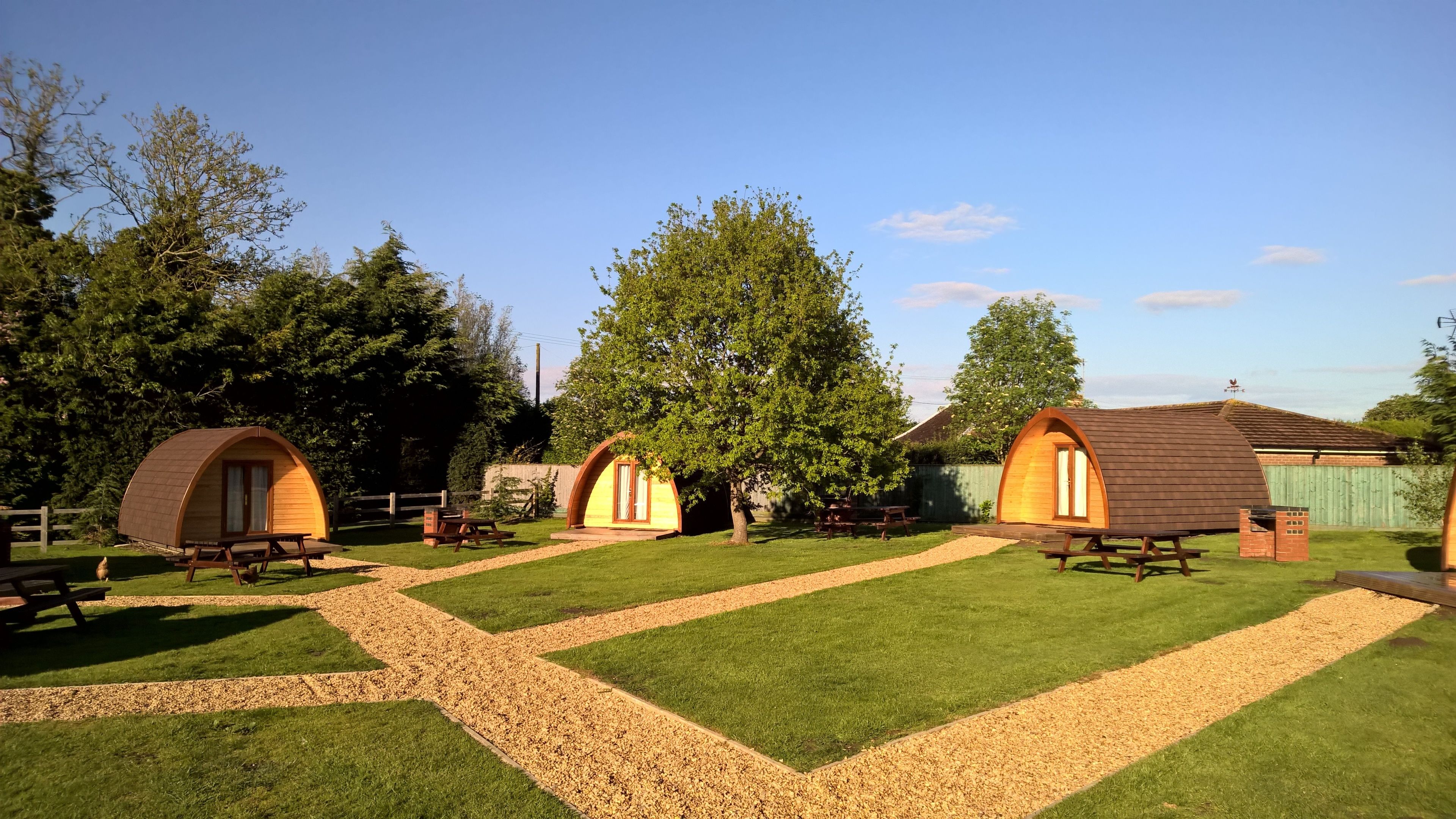 A campsite with several wooden dome-shaped cabins, picnic tables, and a well-maintained lawn.