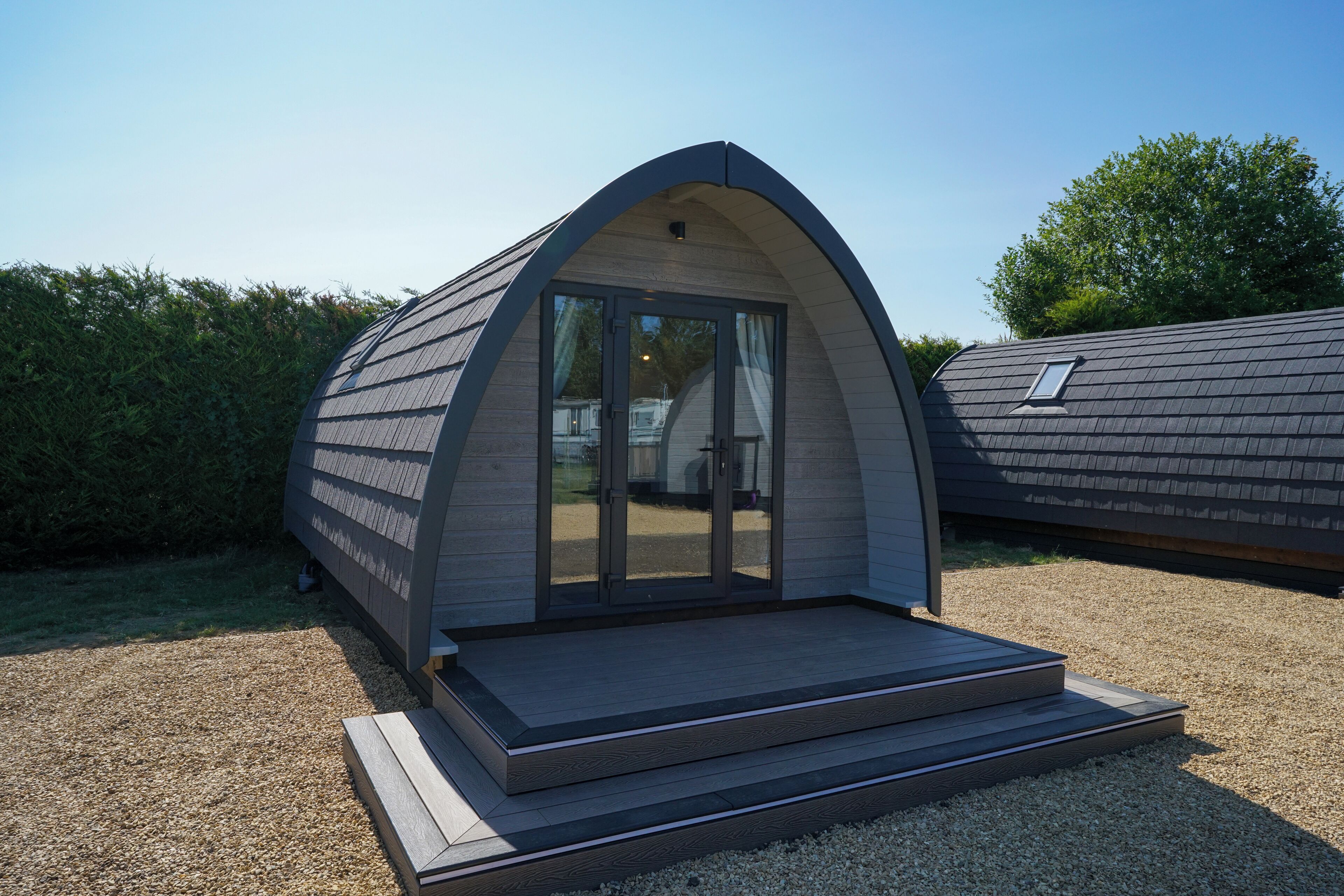 A modern, curved-roofed structure with a glass door entrance and a small outdoor seating area.