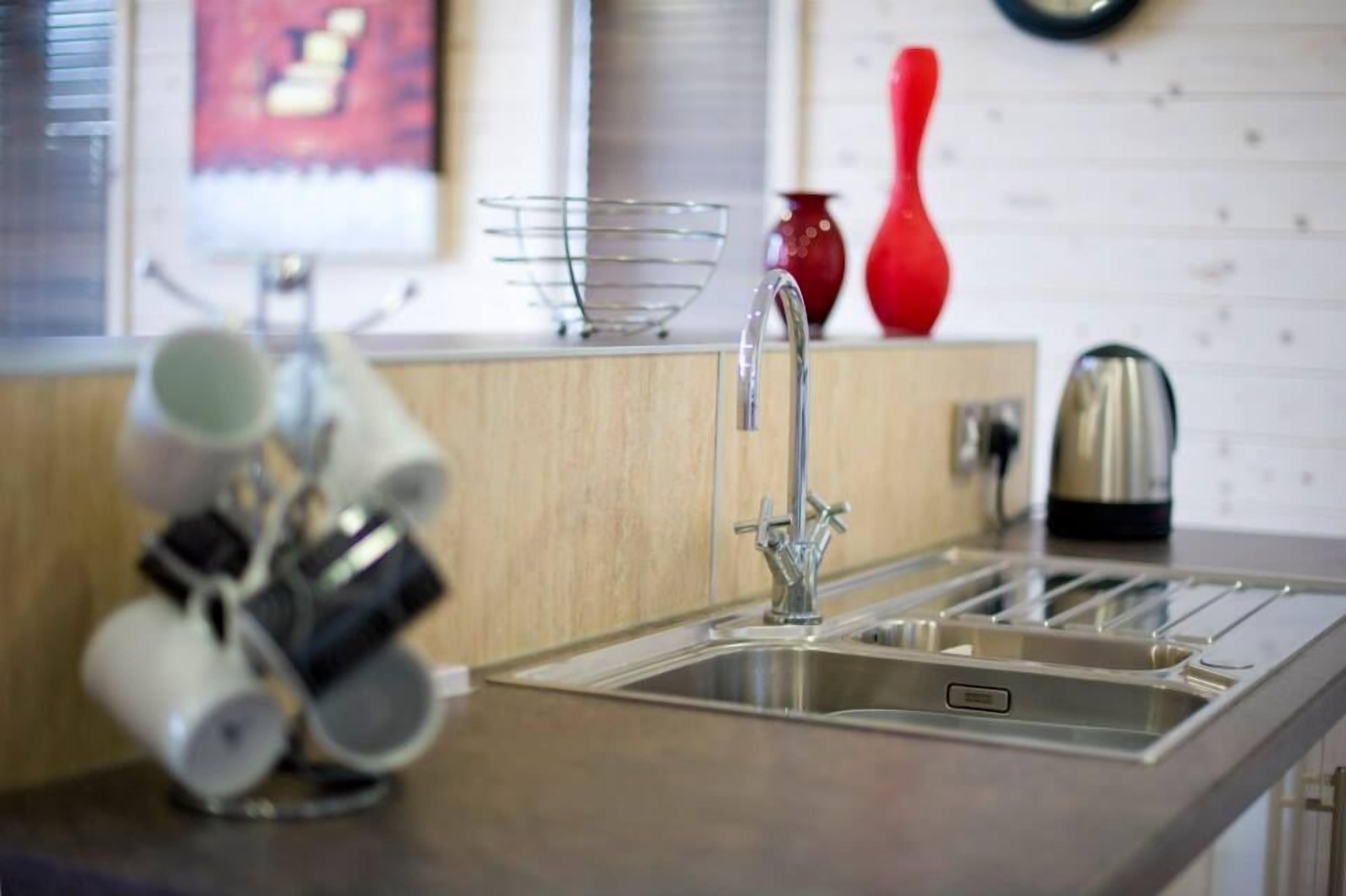 Een keuken met een roestvrijstalen spoelbak, een waterkoker en een rode vaas op het aanrecht.
