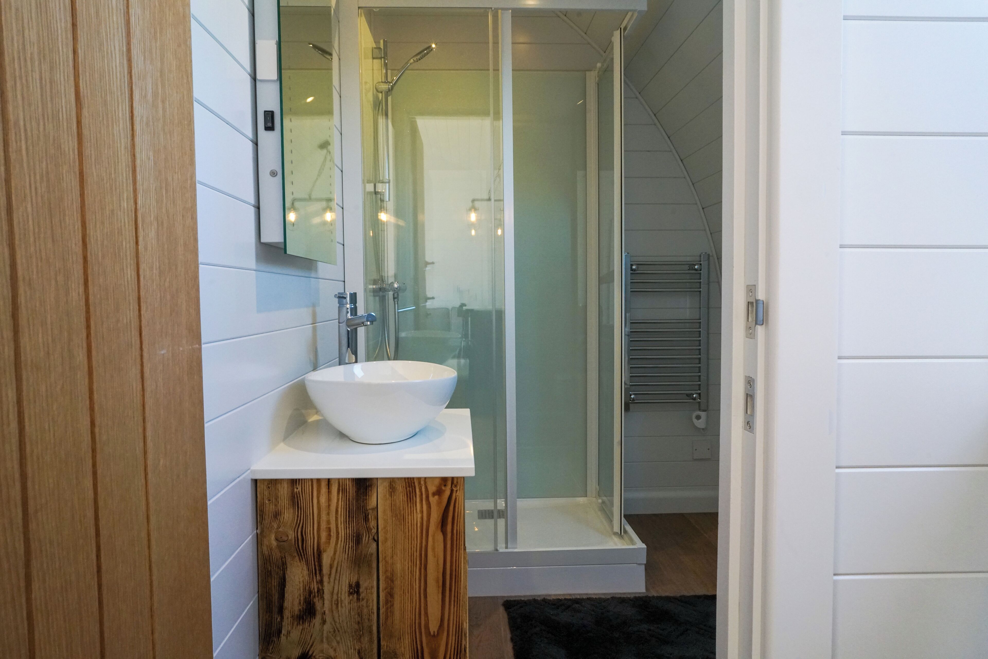 Une salle de bain moderne avec un lavabo blanc, un meuble-lavabo en bois et une cabine de douche en verre.