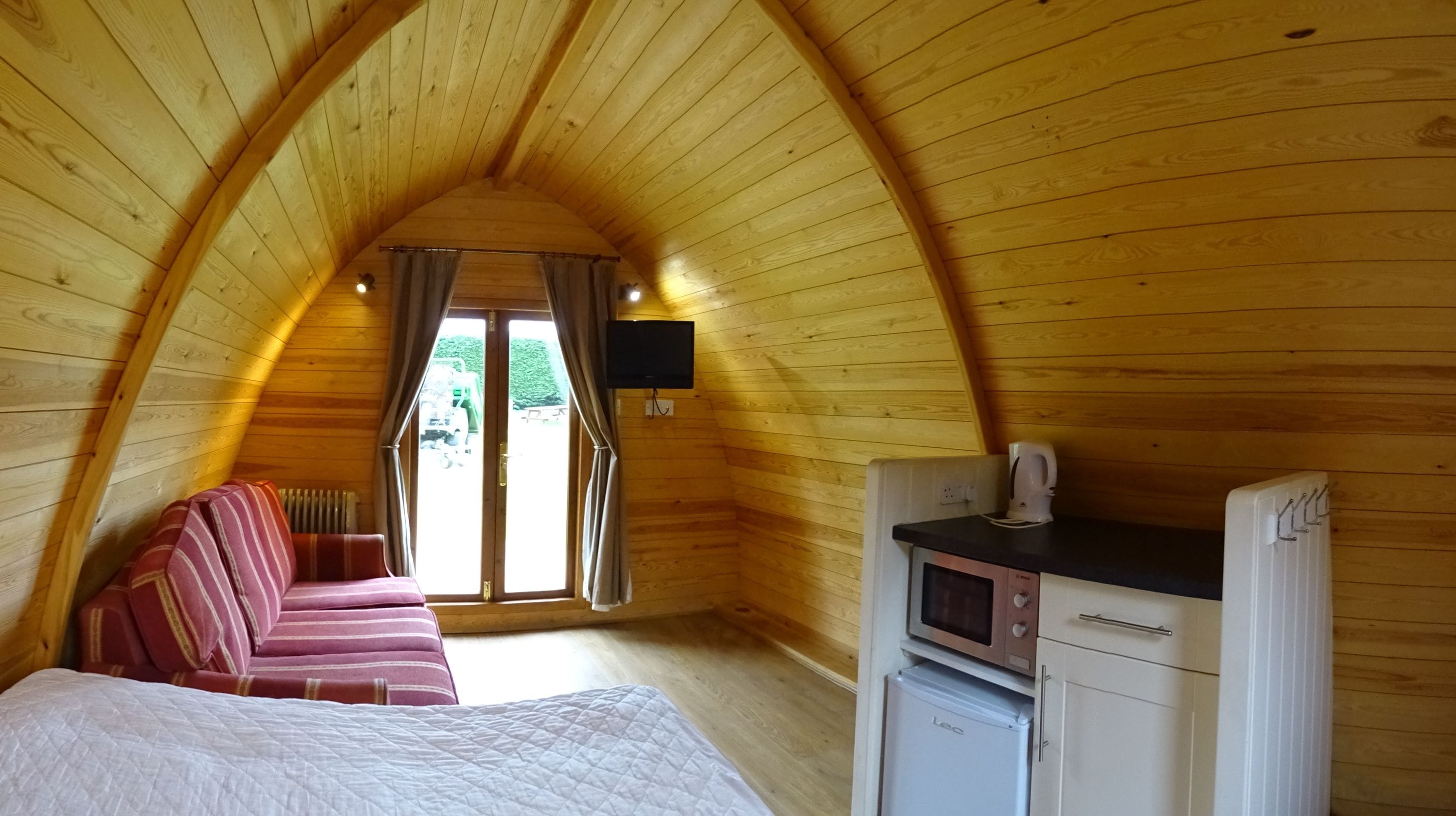 A cozy attic bedroom with a bed, a sofa, a TV, a microwave, and a refrigerator.