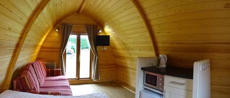 A cozy attic bedroom with a bed, a sofa, a TV, a microwave, and a refrigerator.