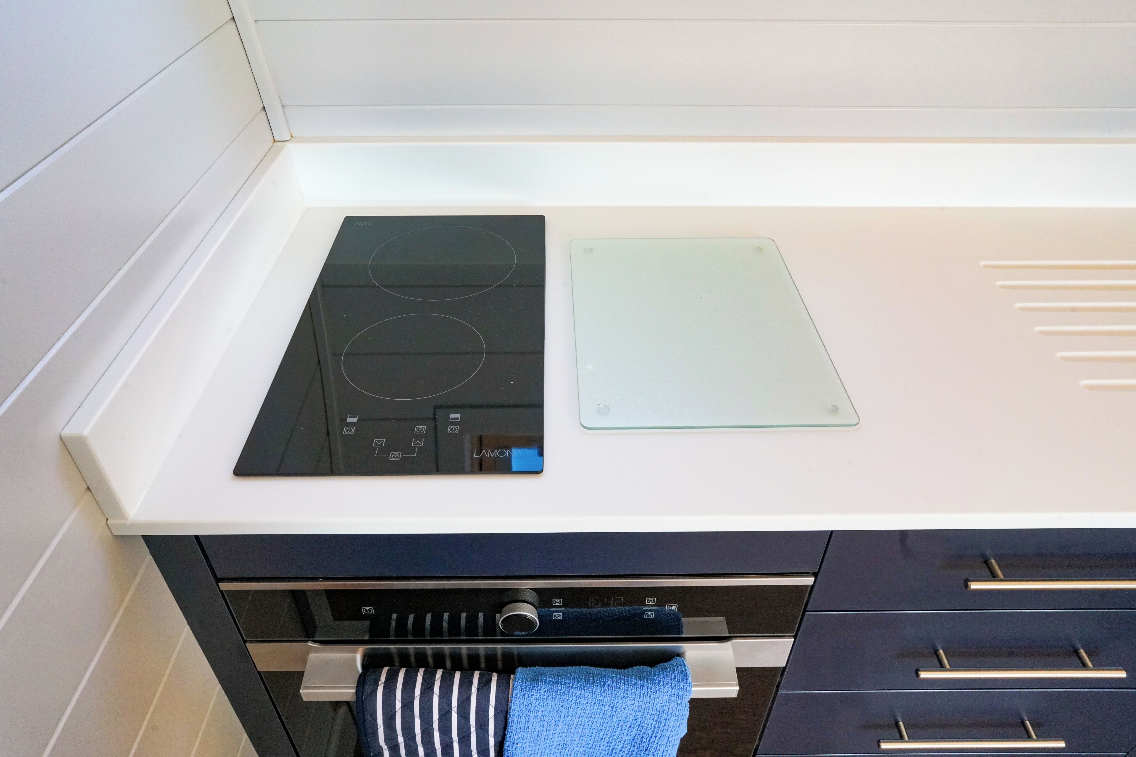 Une cuisine dotée d’une plaque de cuisson à induction noire, d’un plat de cuisson en verre et d’un four en acier inoxydable situé en dessous.