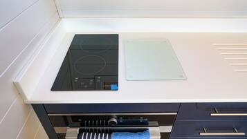 Una cocina con tope de inducción negro, una bandeja de vidrio para hornear y un horno de acero inoxidable debajo.