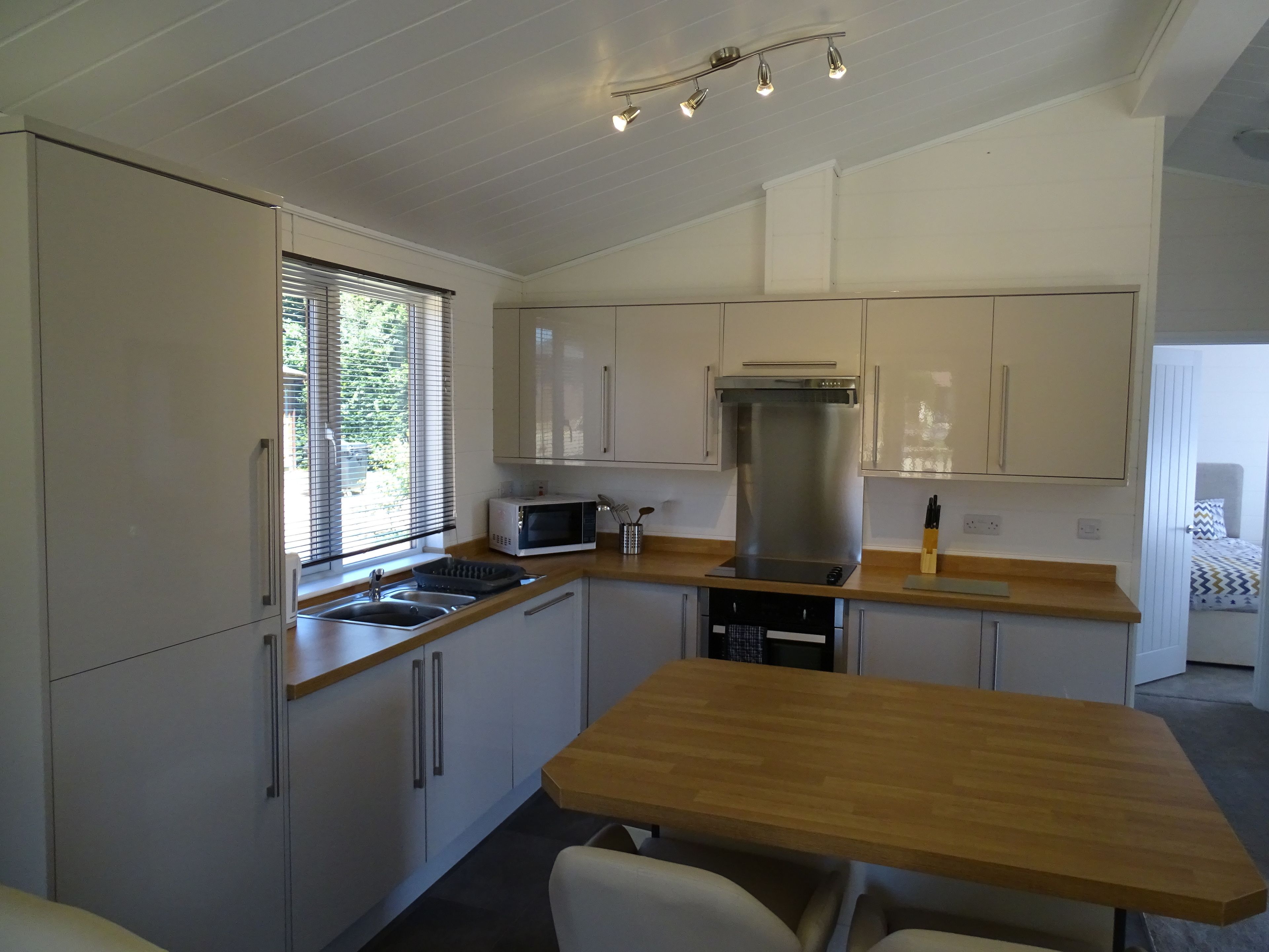 A modern kitchen with white cabinets, a stainless steel range hood, a microwave, and a wooden table.