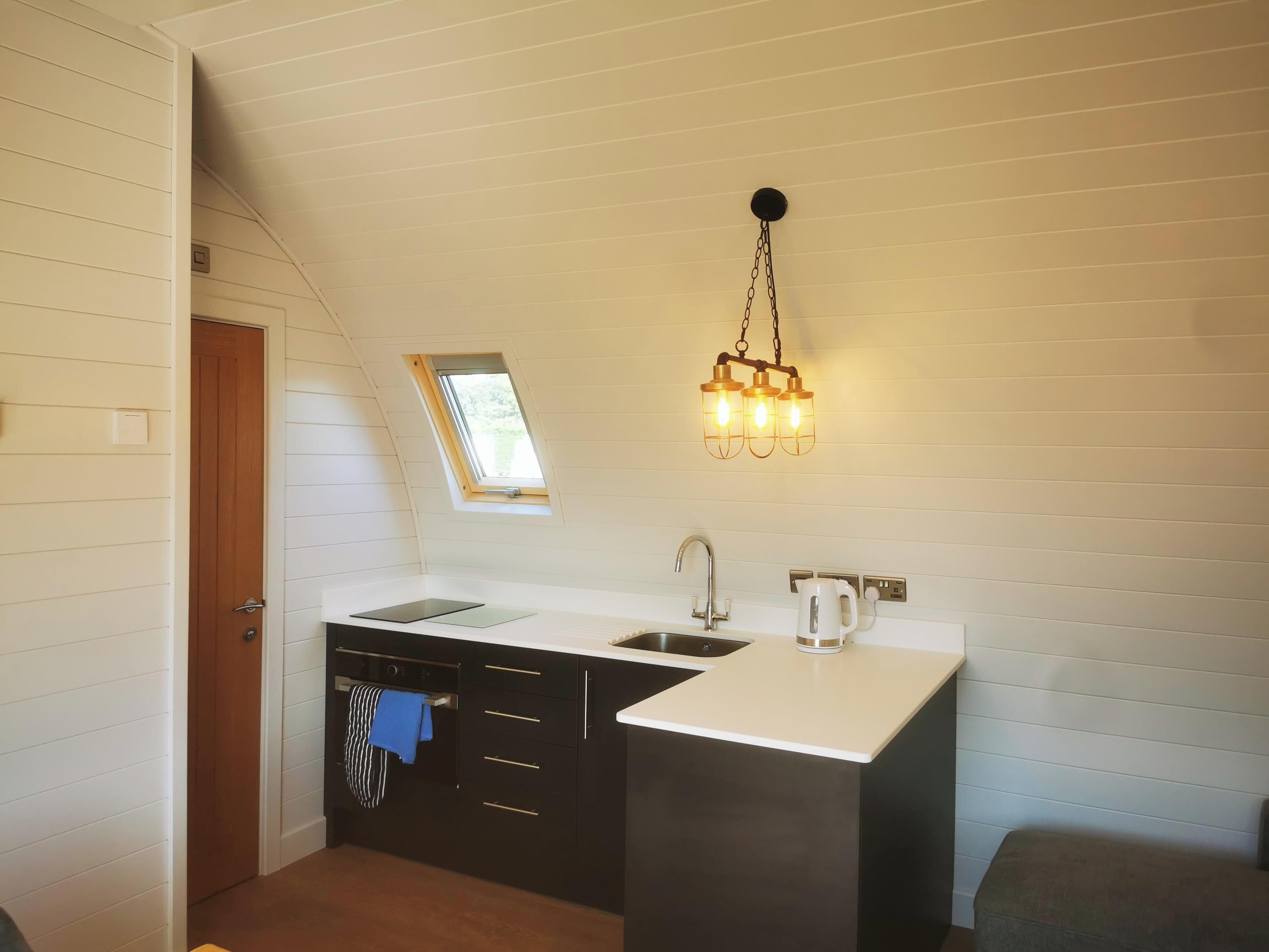 A compact kitchen with a skylight, a hanging light fixture, a built-in oven, and a sink.