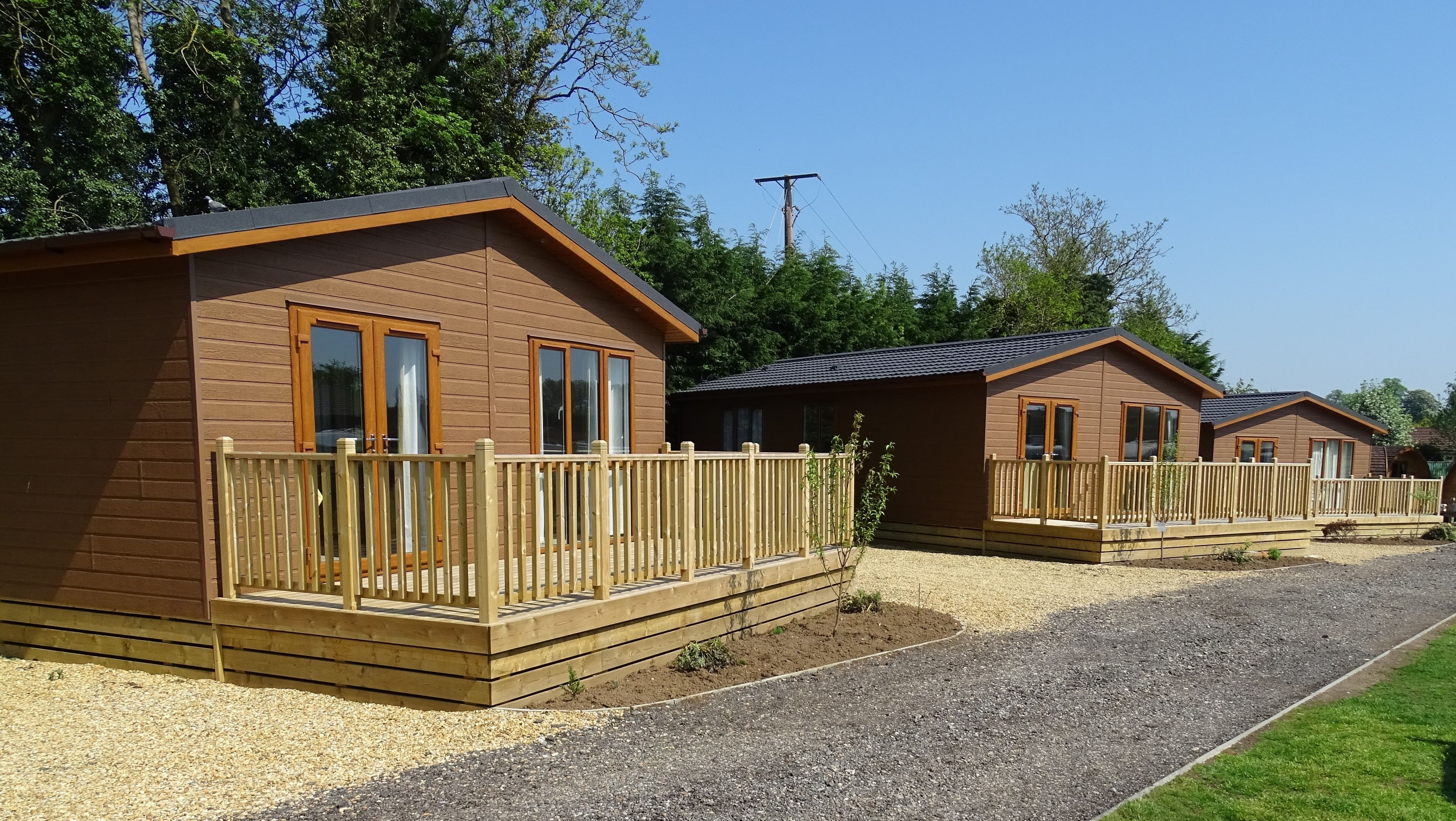 A row of wooden cabins with balconies, surrounded by gravel and grass, under a clear sky.