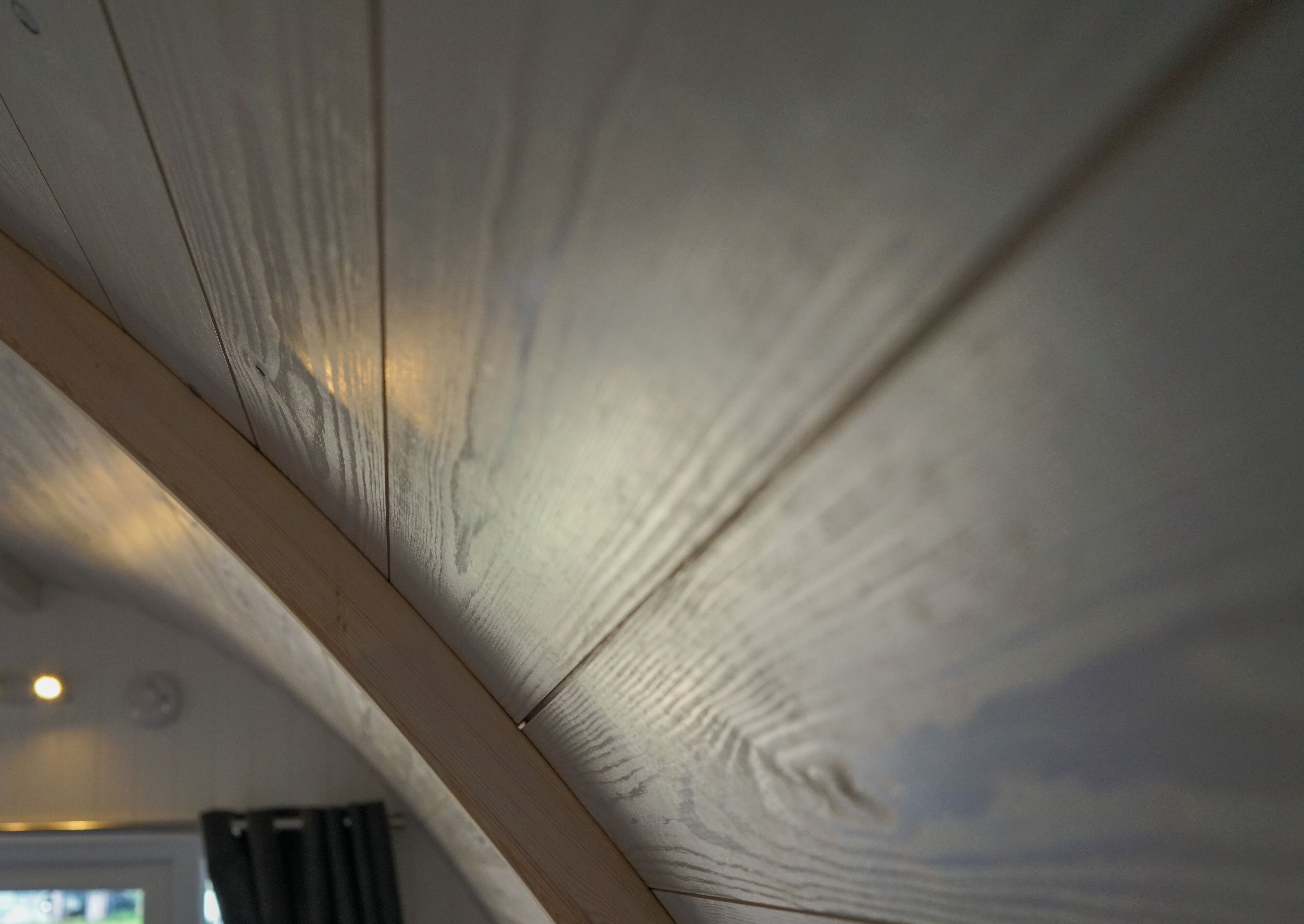 A close-up of a wooden ceiling with visible grain patterns and a light fixture.