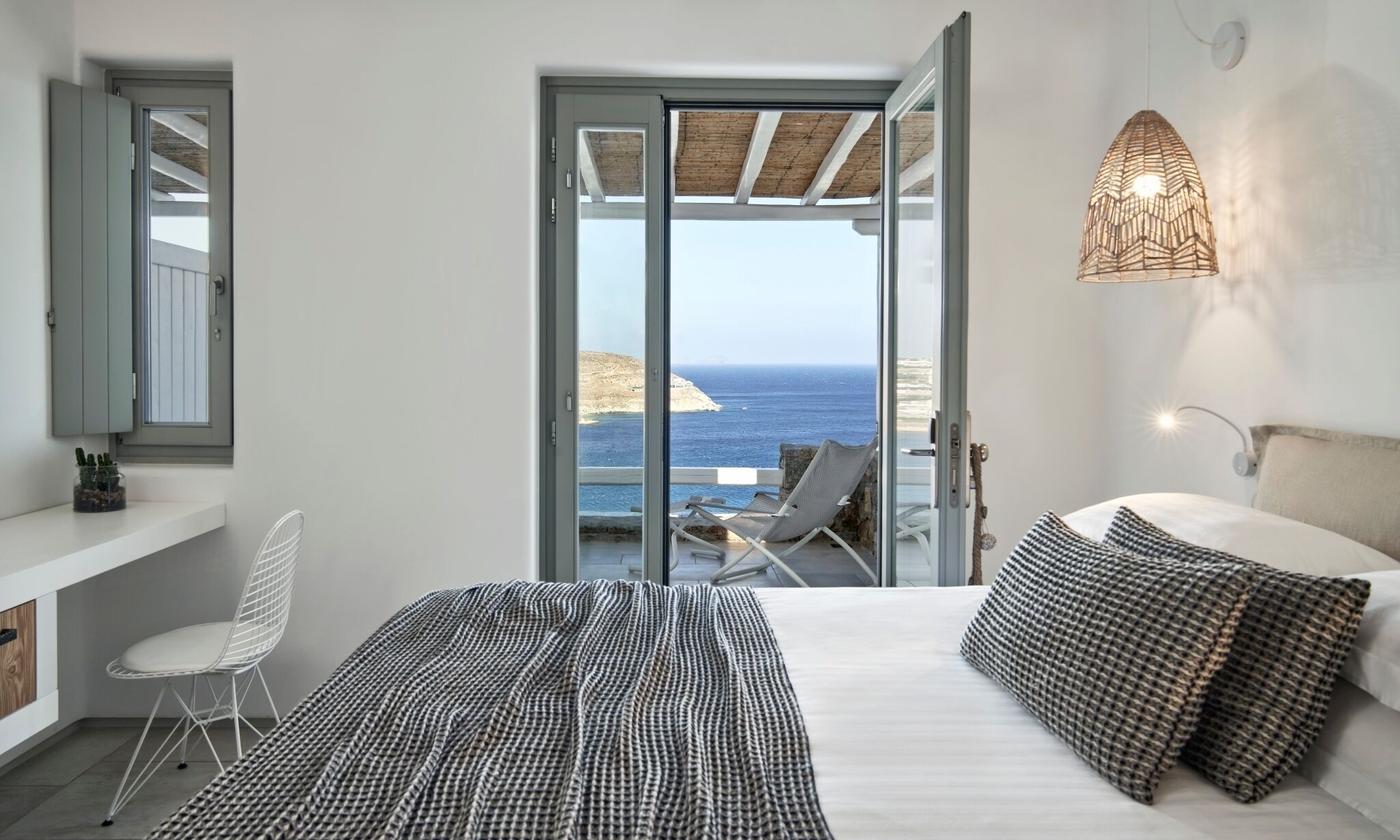 Quarto com cama, cadeira, mesa de cabeceira, luminária e vista para o mar.