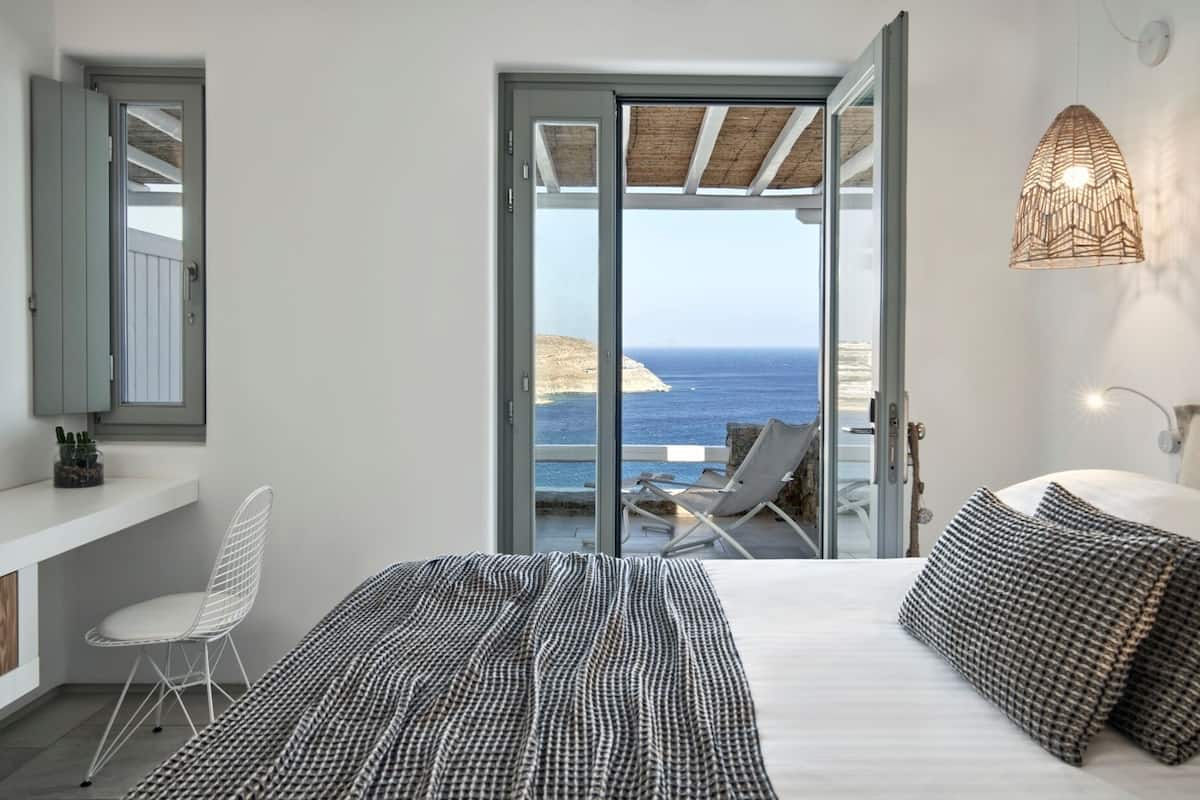 Un dormitorio con cama, una silla, una mesita de noche, una lámpara y vistas al mar.