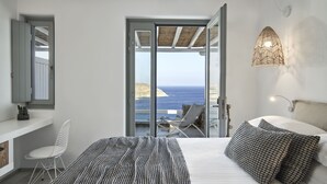 Een slaapkamer met een groot bed, uitzicht op zee, een balkon met een stoel en een hanglamp.