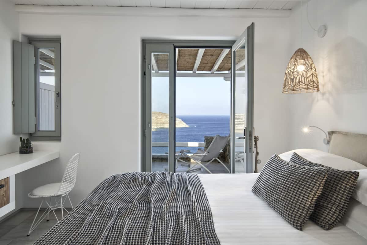 Een slaapkamer met een groot bed, uitzicht op zee, een balkon met een stoel en een hanglamp.