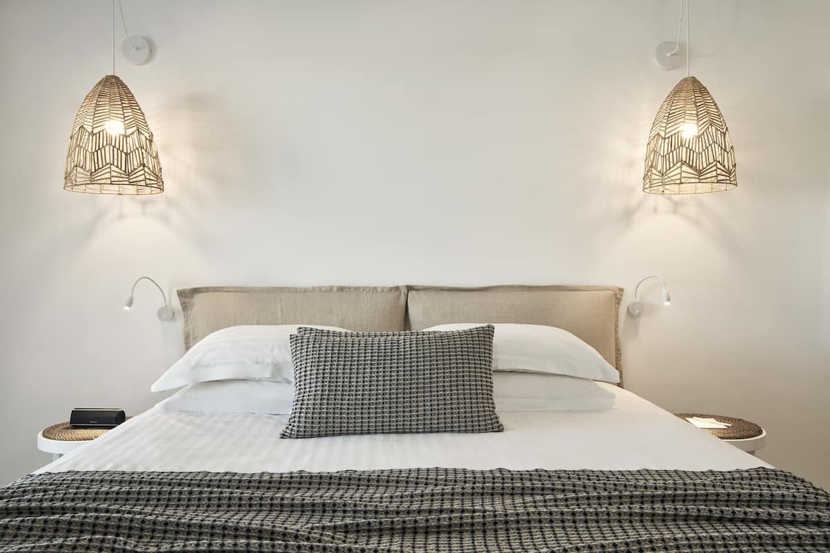 Een net opgemaakt bed met een geruite deken, twee hanglampen en een nachtkastje met een lamp.