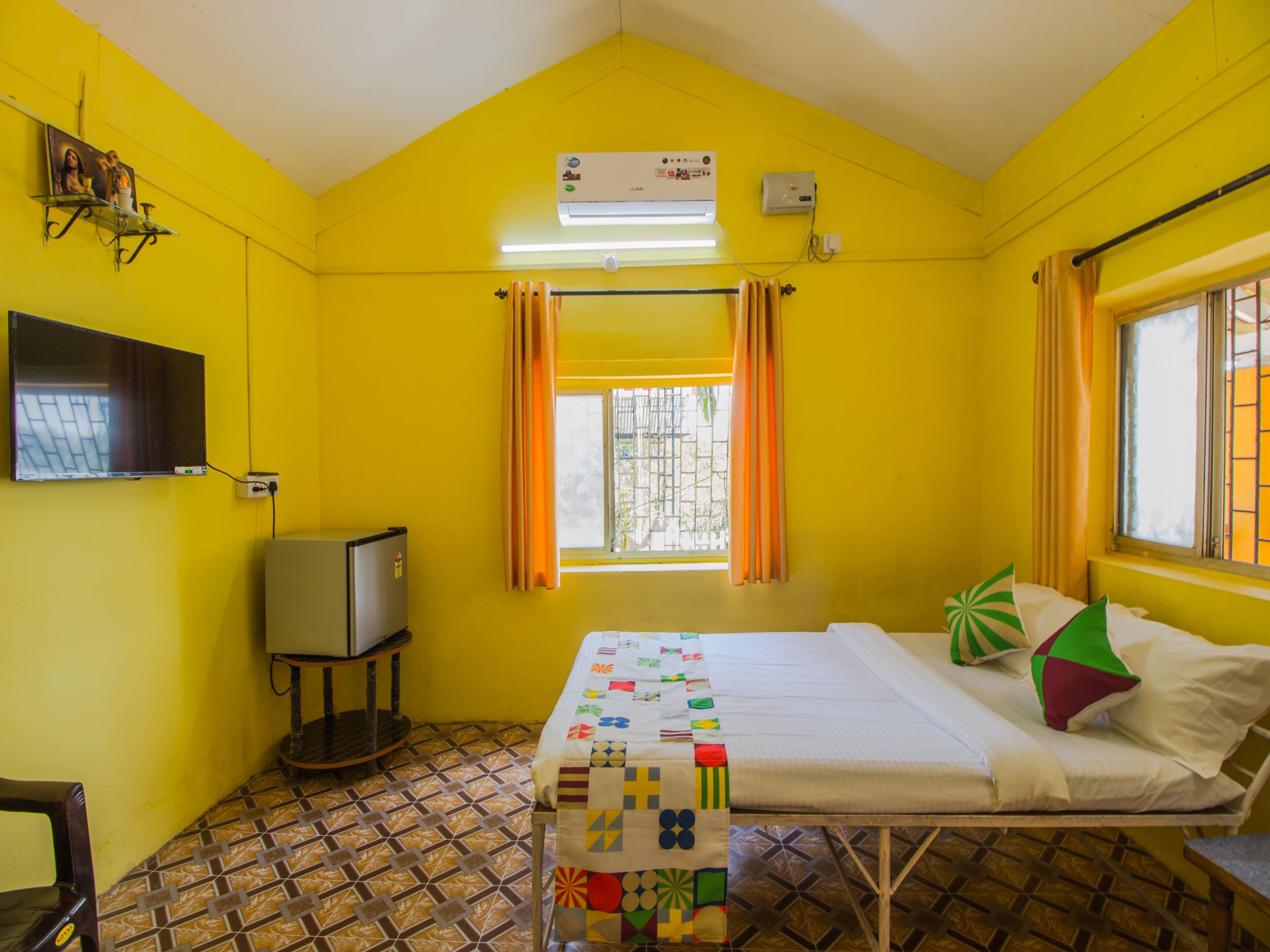 A small, brightly colored room with a bed, a television, and a window with curtains.