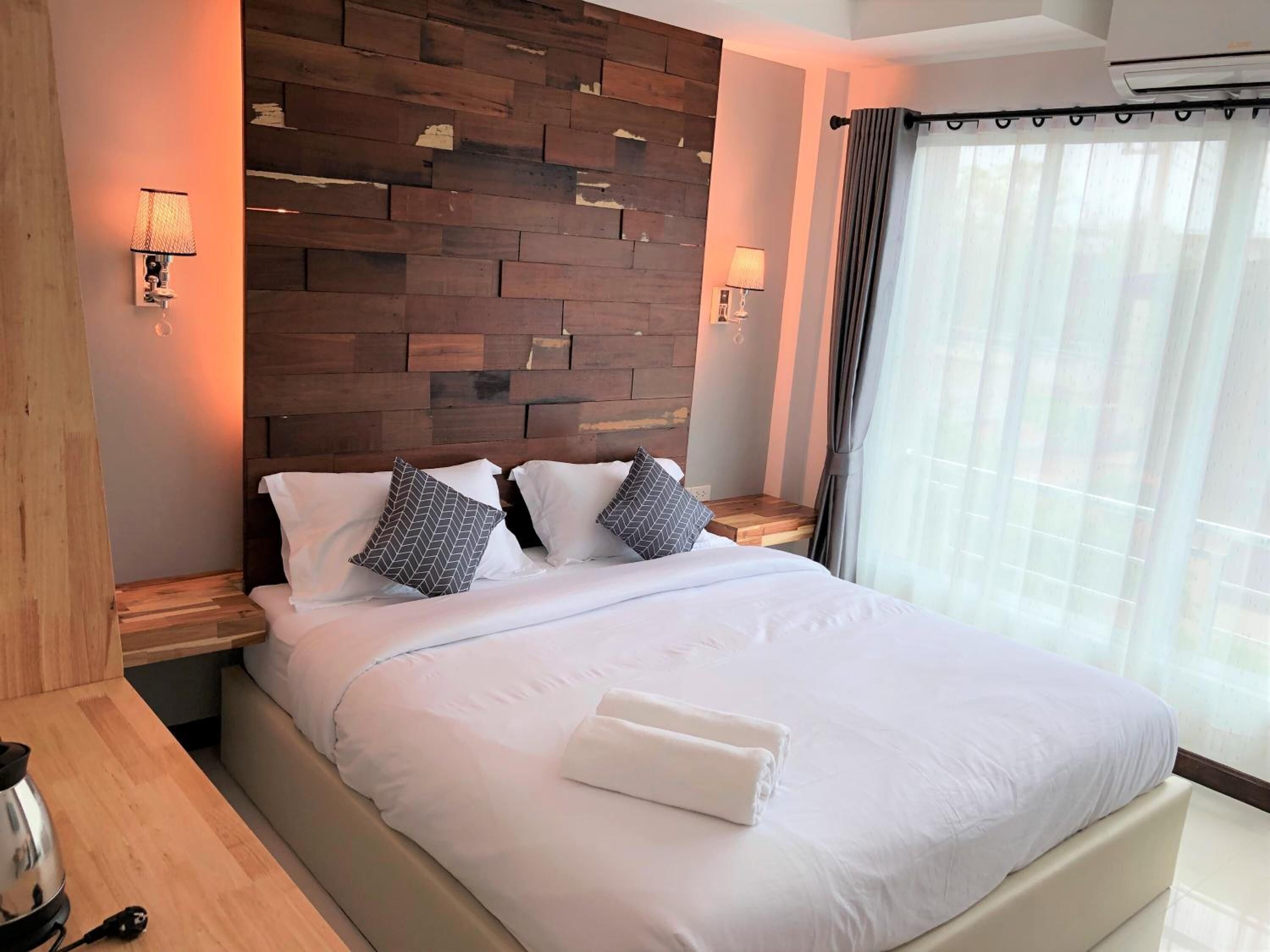 A hotel room with a wooden headboard, a bed with white linens, two bedside lamps, and a window with curtains.