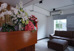 A reception area with a wooden counter, a brown leather sofa, and a window with a view of greenery. - Nan Panwa Hotel (Nan)
