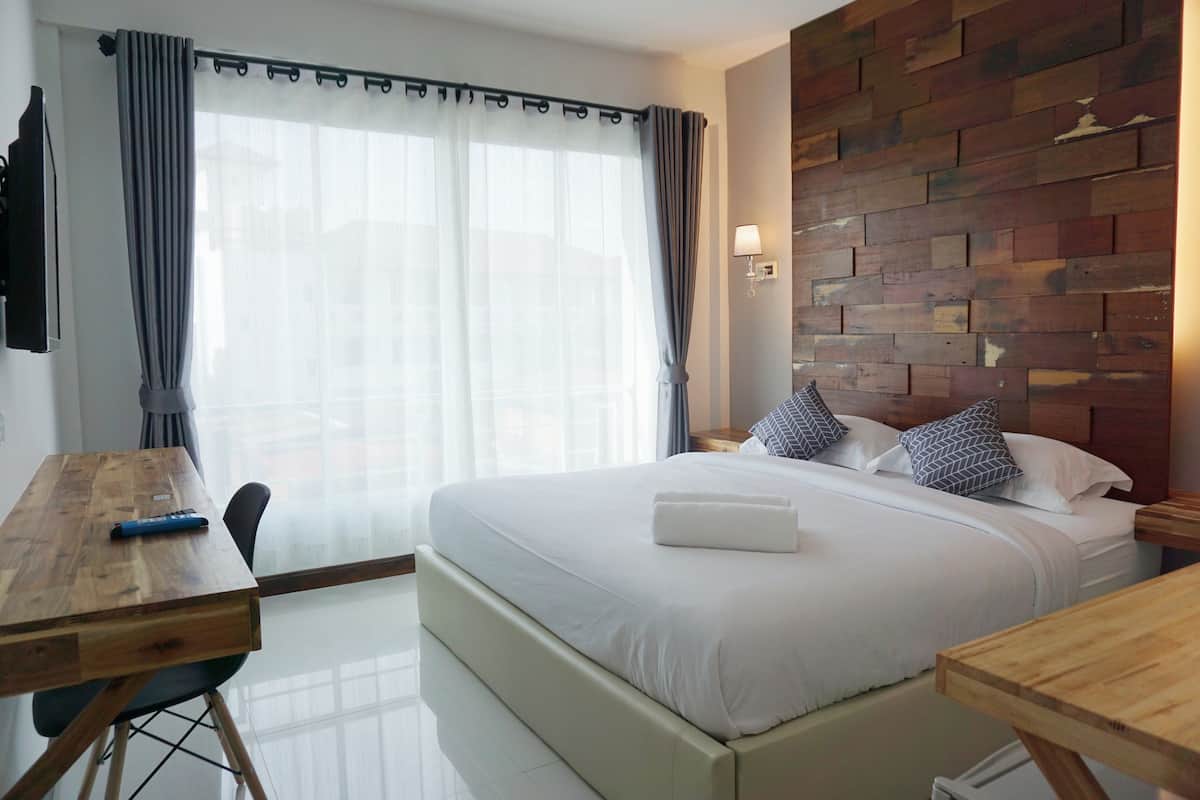 A hotel room with a large bed, a wooden desk, a modern light fixture, and a brick-patterned wall.