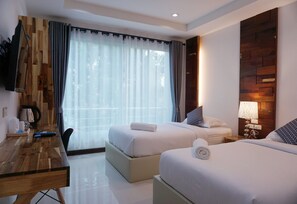 A hotel room with two beds, a wooden desk, a flat-screen TV, and a large window with curtains. - Nan Panwa Hotel (Nan)