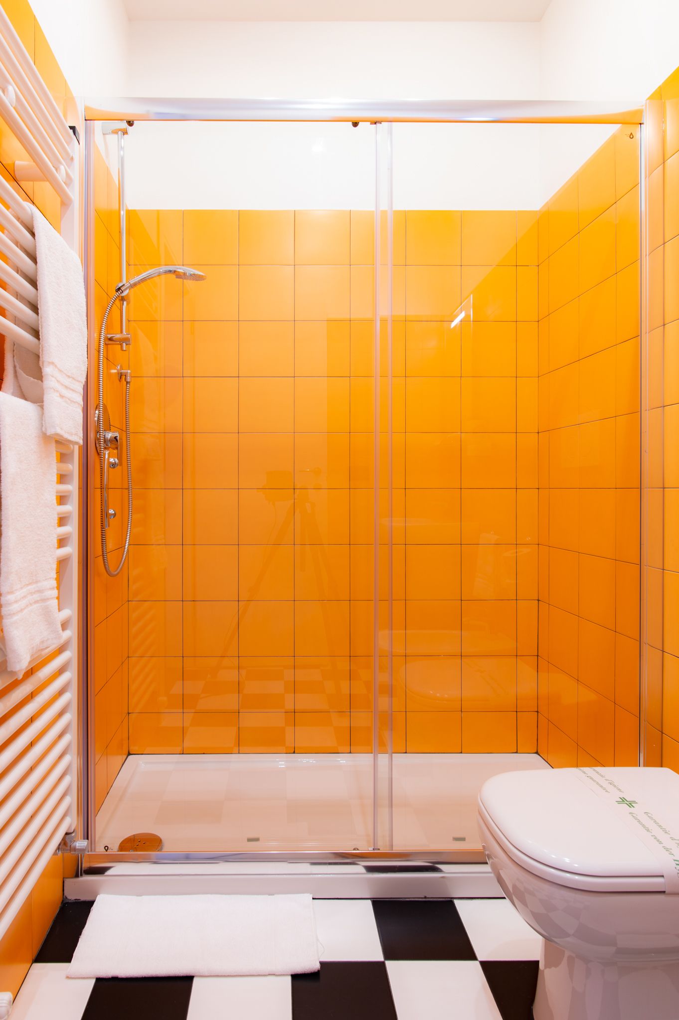 Een badkamer met een douche met glazen wand, een wit toilet en oranje betegelde muren.