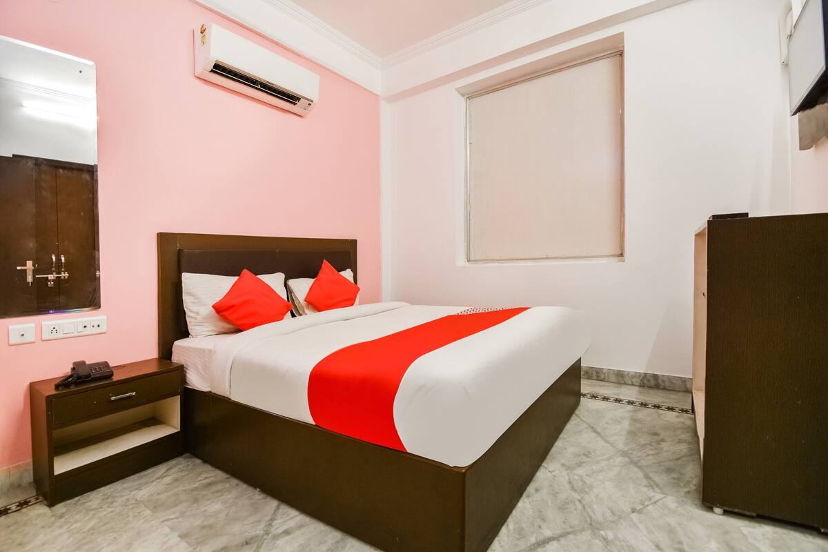 A bedroom with a bed, a nightstand, a wardrobe, a window, and an air conditioning unit.
