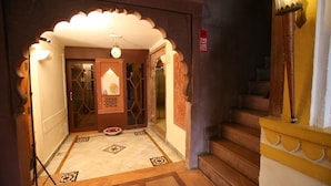 Un couloir orné d’une arche de style traditionnel, avec un escalier et un panneau d’avertissement indiquant la présence d’un système de vidéosurveillance.