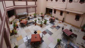 Une cour dotée de nombreuses tables et chaises, entourée de plantes en pot et agrémentée d’une fontaine centrale.