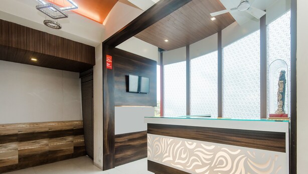 Uma área de recepção com um banco de madeira, um balcão de atendimento com painel decorativo, uma televisão e uma janela ampla com vista para o céu.