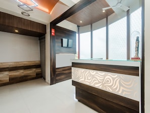 A reception area with a wooden bench, a reception desk with a decorative panel, a television, and a large window with a view of the sky.