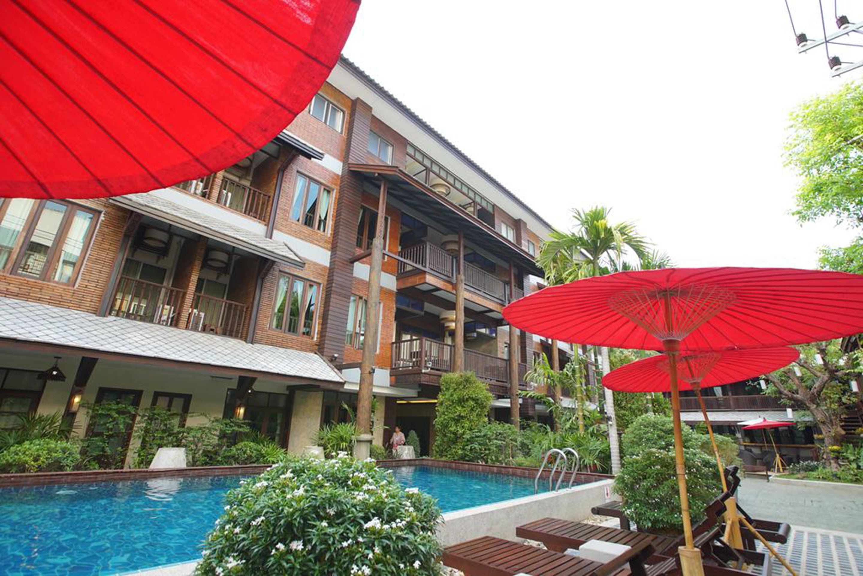 A hotel with a pool, outdoor seating, and a red umbrella.