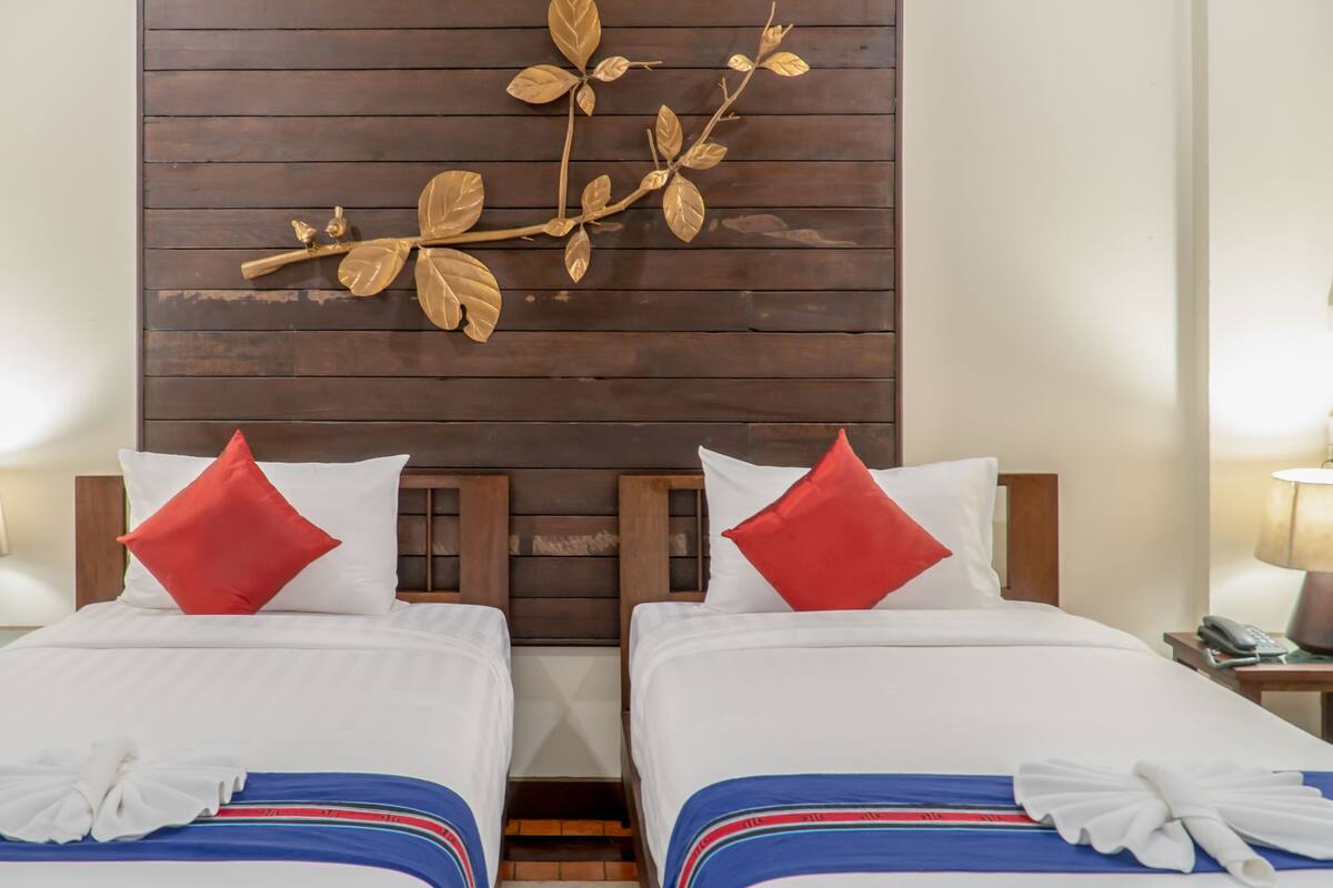 A hotel room with two beds, each with white bedding and red pillows. There is a wooden headboard with a decorative branch above the beds.