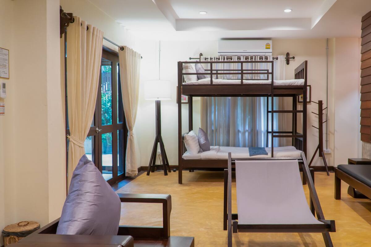 A room with a bunk bed, a sofa, a table, and a bench.