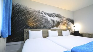 Una habitación de hotel con una cama grande, un escritorio y un televisor montado en la pared.