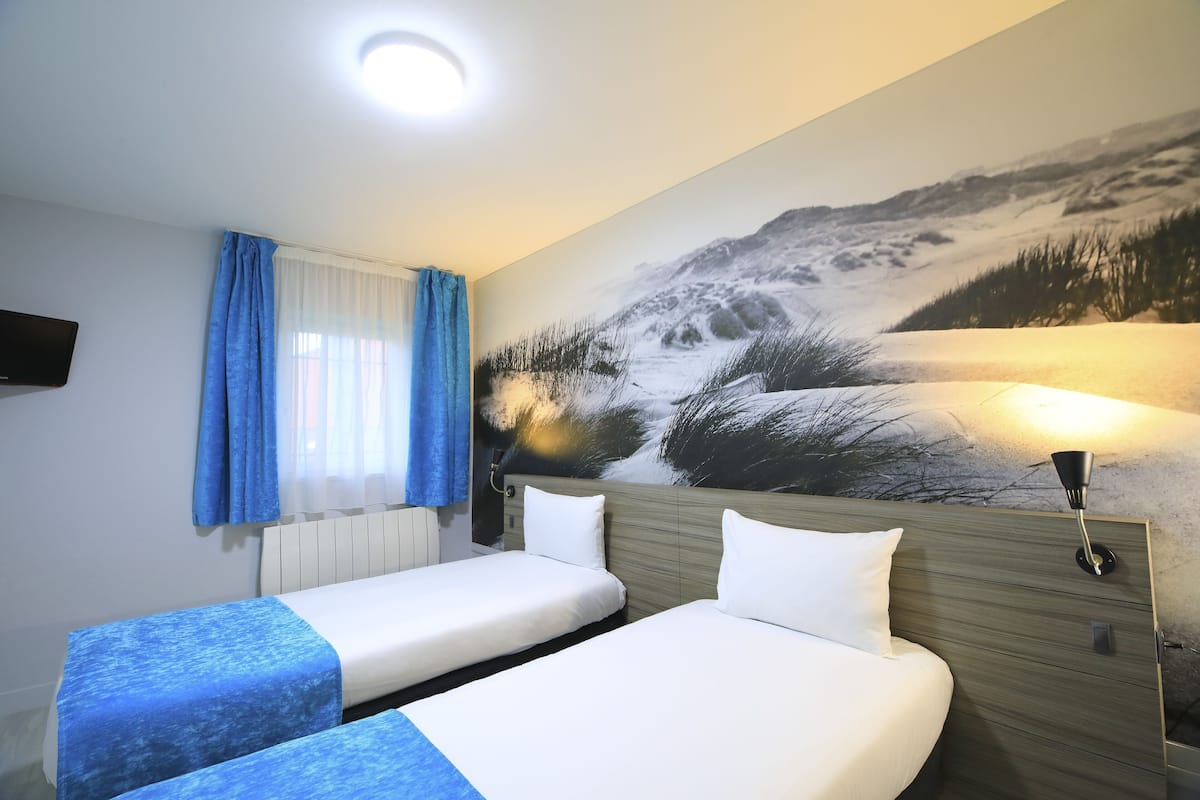 Une chambre d’hôtel avec deux lits, une grande fresque murale, un téléviseur à écran plat et une fenêtre avec des rideaux bleus.