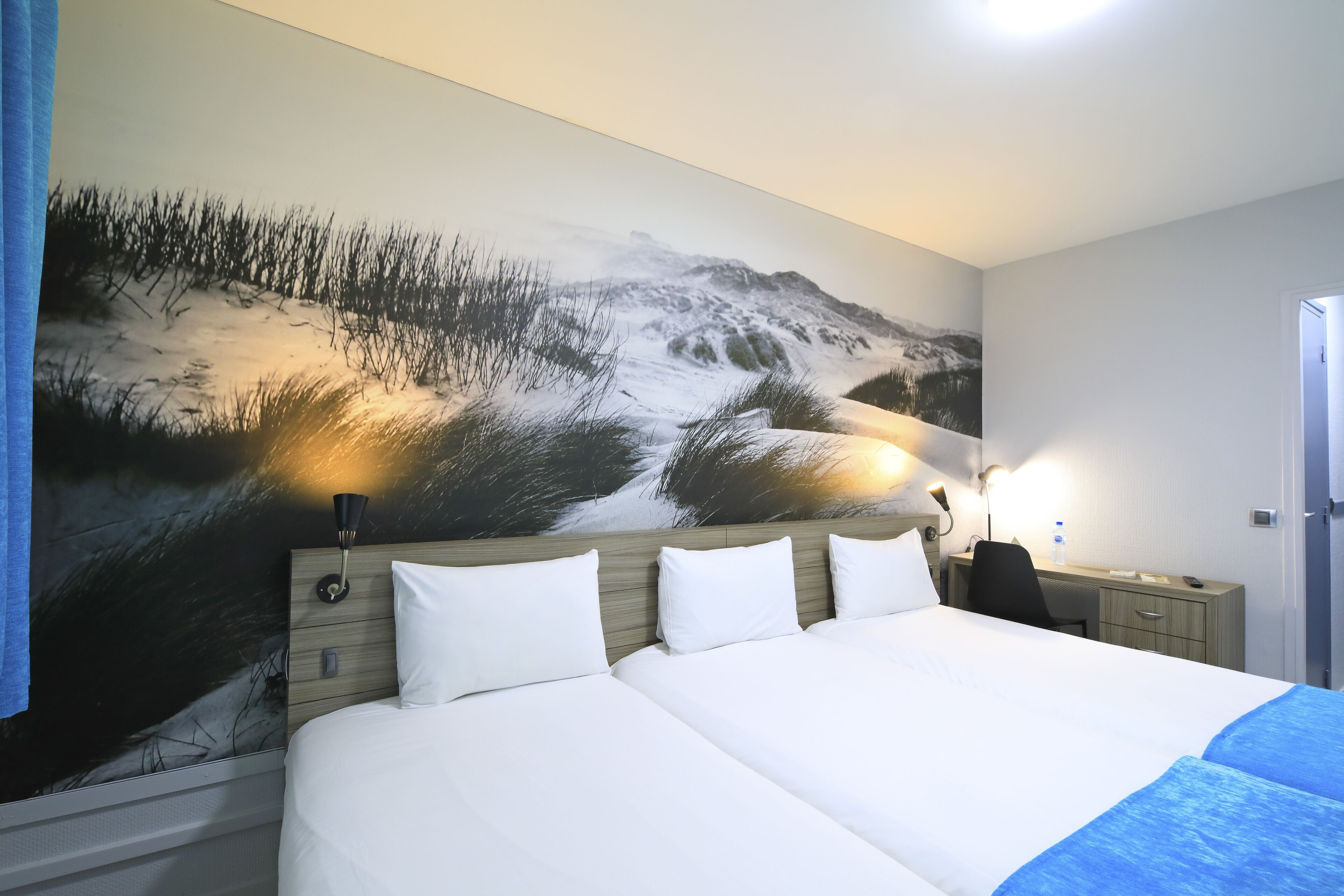 Habitación de hotel con una cama grande, un escritorio, una silla y un mural en la pared que representa un paisaje nevado.