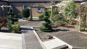 Una terraza de madera con jardín, que incluye varios arbustos y un pérgola.