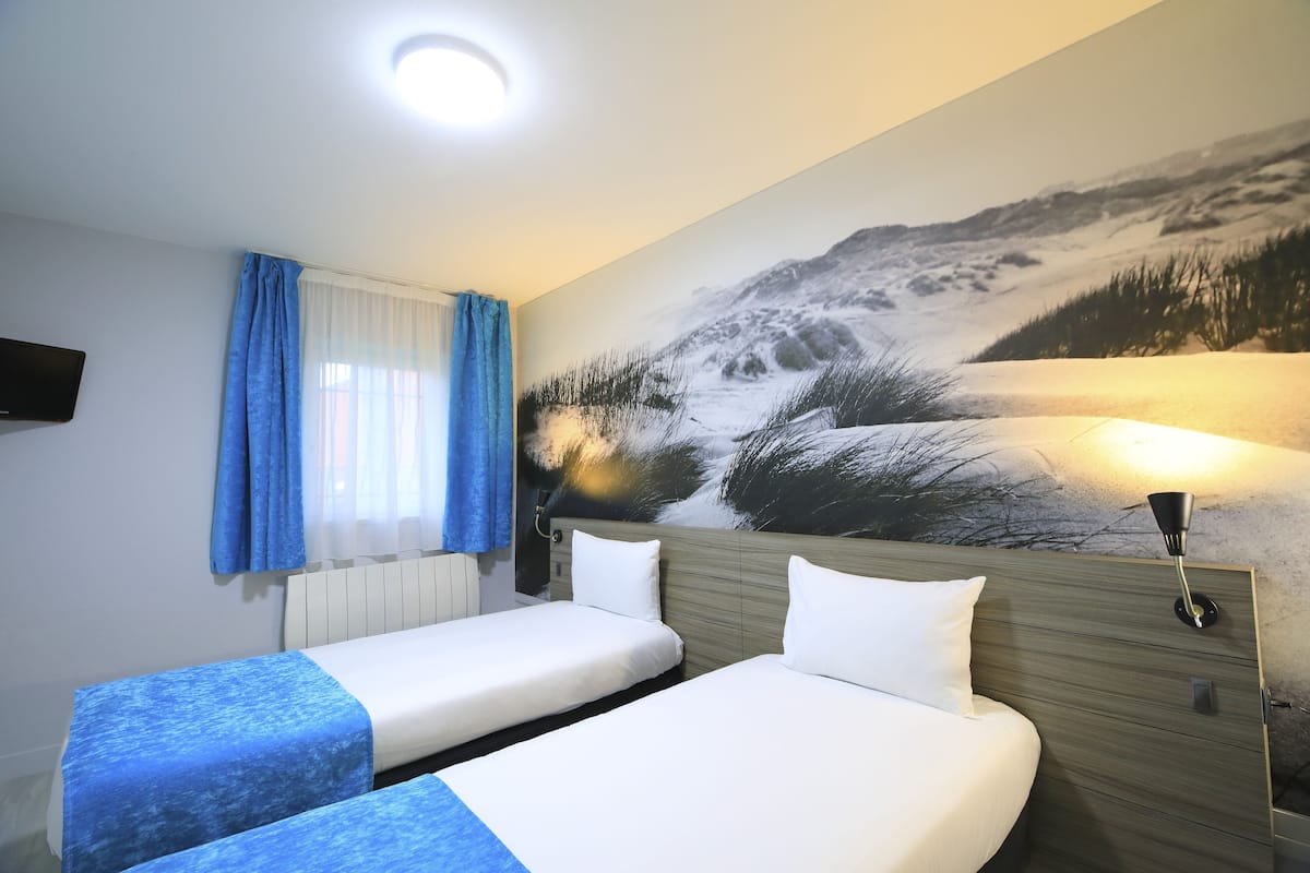 Une chambre d’hôtel avec deux lits, une grande fresque murale, un téléviseur à écran plat et une fenêtre avec des rideaux bleus.