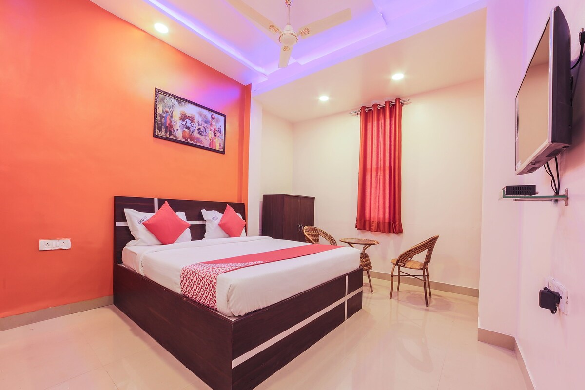 A hotel room with a bed, a small table, two chairs, a TV, and a painting on the wall.