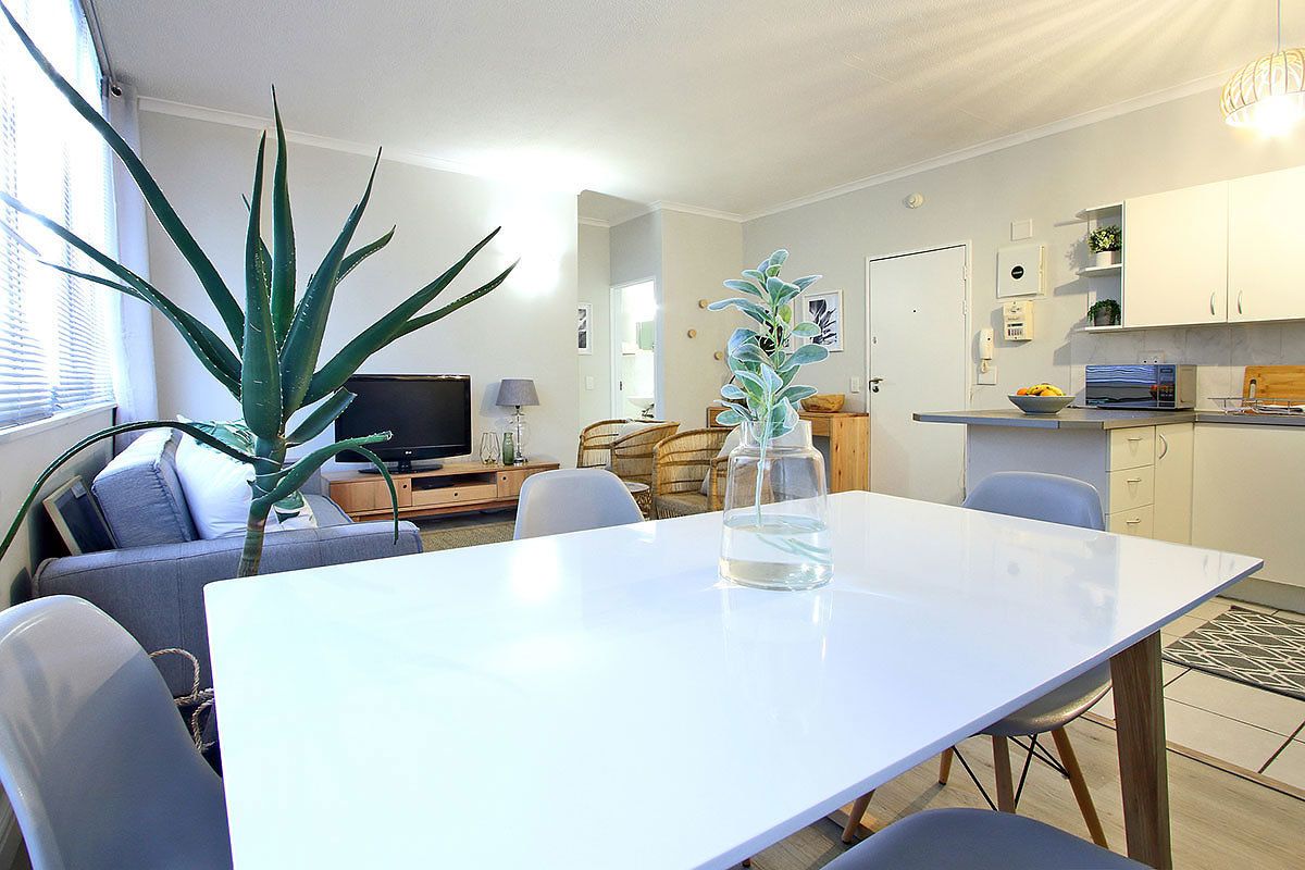 Ett modernt vardagsrum med ett vitt bord, en grå soffa och en stor, grön växt.