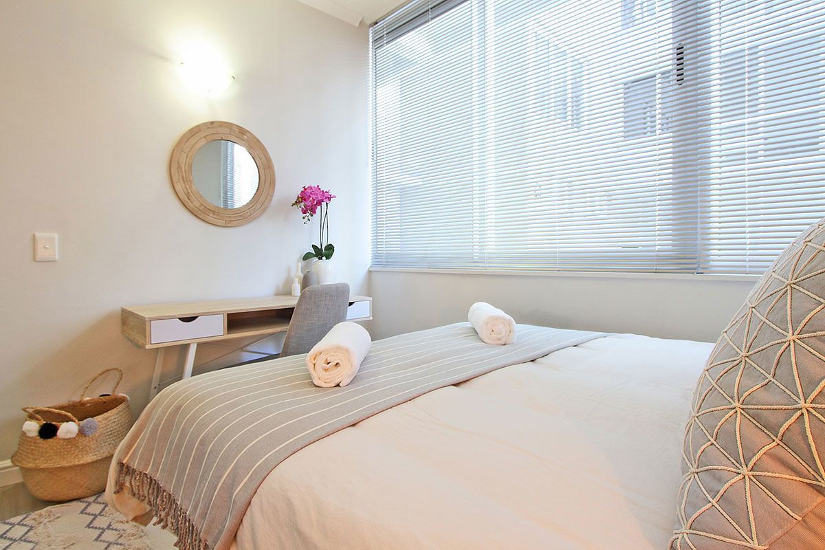 Une chambre à coucher comprenant un lit, un bureau, une chaise, un miroir et une fenêtre avec des stores.