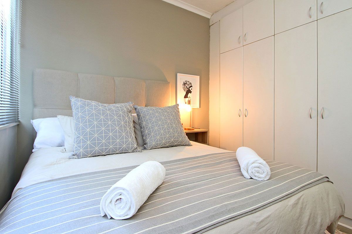 A neatly made bed with striped bedding and geometric pillows, a rolled towel on the bed, and a wardrobe with silver handles.