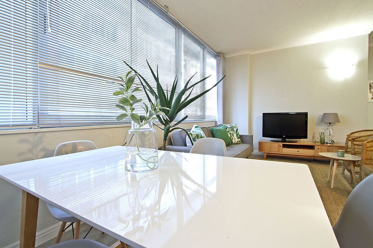 A modern living room with a white table, a television, and a plant.