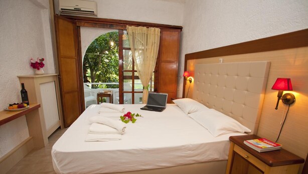 A neatly made bed with a laptop, a bedside table with a book, and a view of greenery outside. - Damnoni Paradise (Agios Vasileios)