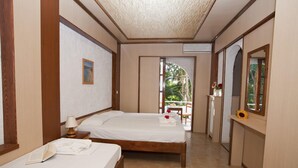 A hotel room with two beds, a wooden floor, a small table with a lamp, and a view of the outdoors. - Damnoni Paradise (Agios Vasileios)
