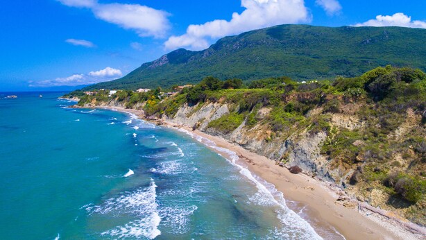 A coastal landscape with a beach, ocean, and a mountain in the background. - Villa Angela (Corfu)